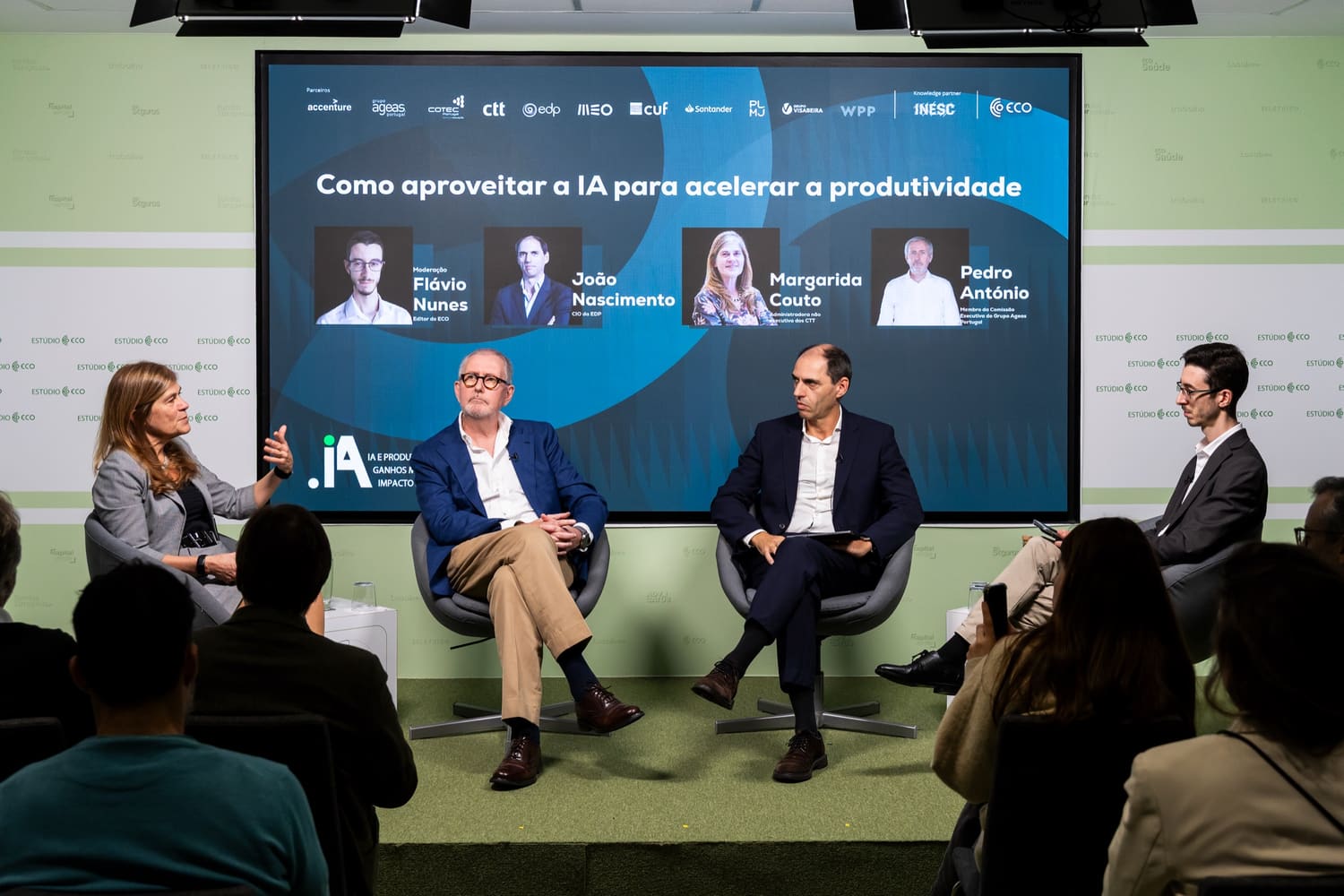 Painel numa conferência, quatro pessoas em palco diante de uma plateia.